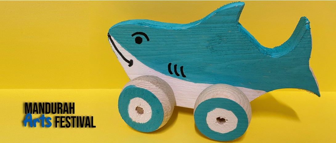 A blue and white shark toy made of wood and on wheels, sits against a bright yellow background
